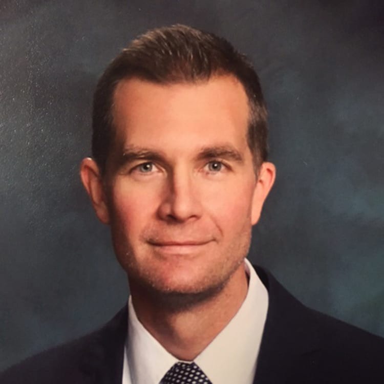 a man wearing a suit and tie smiling and looking at the camera
